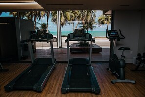 A gym with treadmills and an exercise bike, overlooking a beach with palm trees. - Unity #122 - Apartamento by Carpediem (João Pessoa)