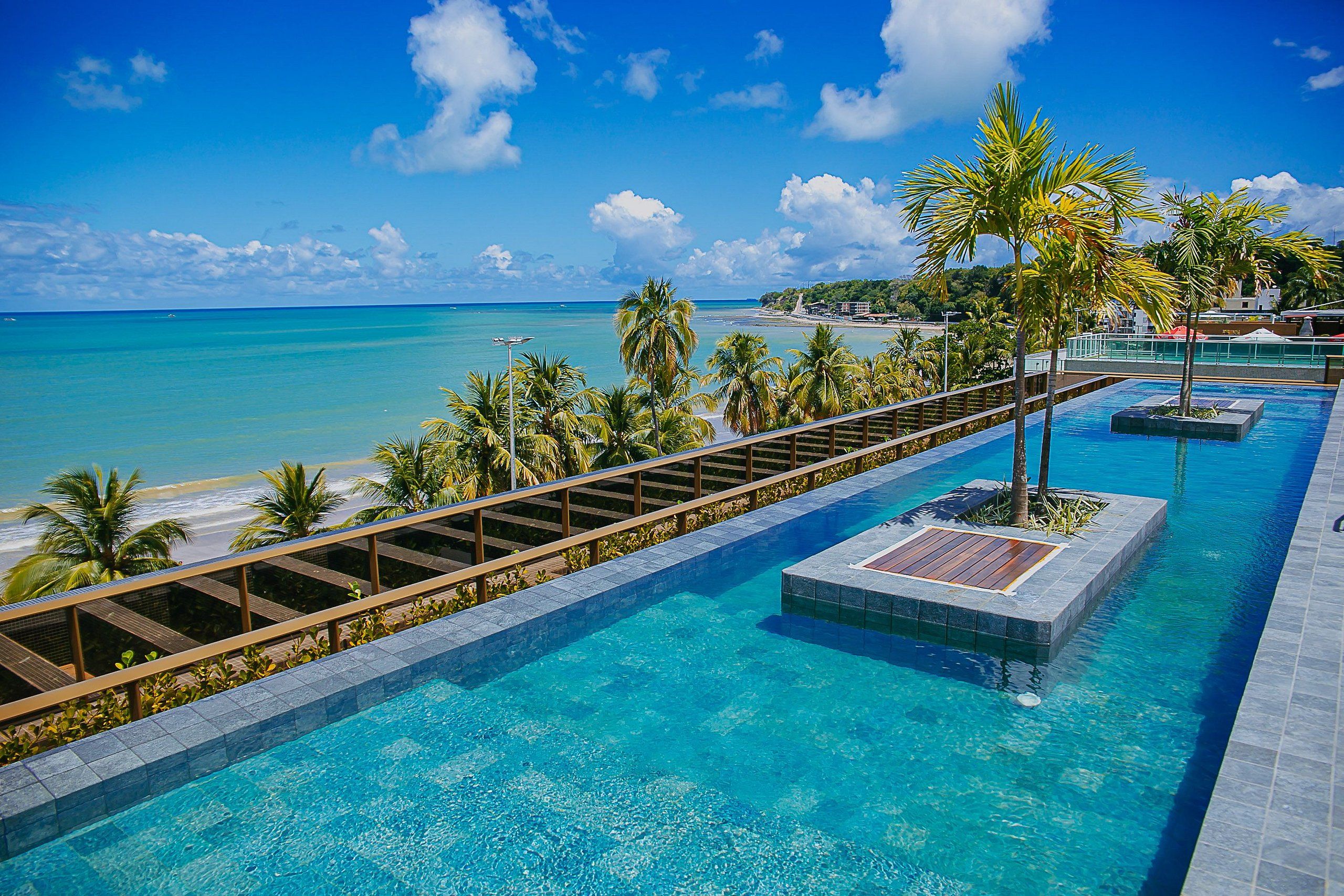 A pool with clear blue water, surrounded by palm trees and a view of the beach.