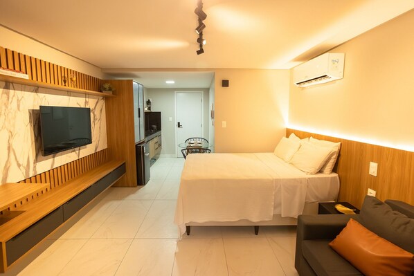 Ein modernes Hotelzimmer mit einem Bett, einem an der Wand befestigten Fernseher, einer Holzkonsole und einer kleinen Sitzecke.