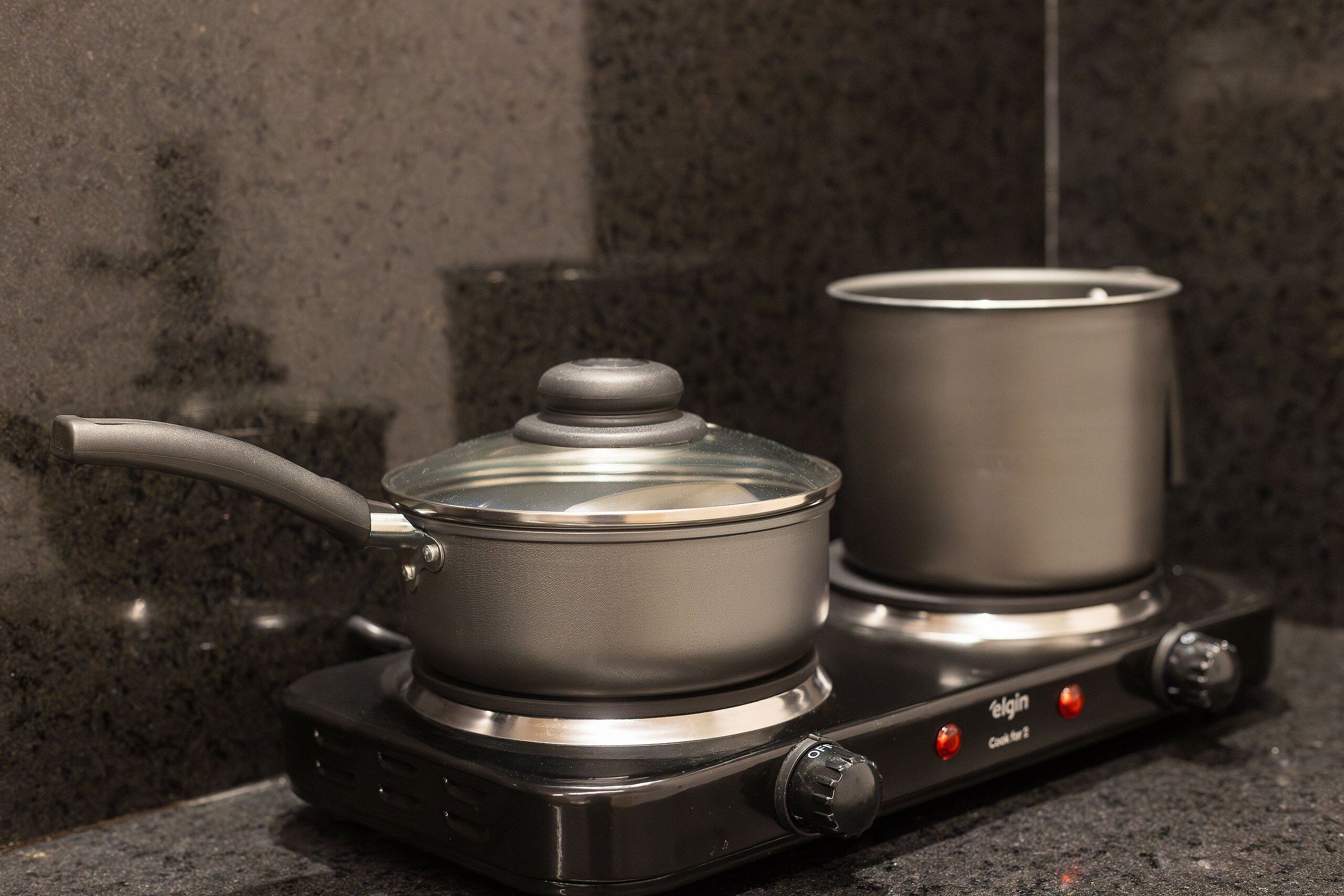 A portable electric stove with two pots on it, set against a dark granite countertop.