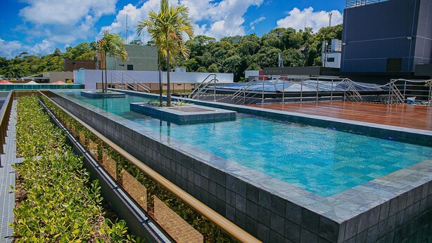 A swimming pool with a tiled edge, a wooden deck, and a view of buildings and trees in the background. - Unity #222 a Few Steps From the Beach by Carpediem (João Pessoa)