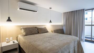 Una camera d'albergo moderna con un letto grande, due lampade a sospensione, un condizionatore d'aria, un comodino con una lampada e vista all'esterno tramite un'ampia finestra.