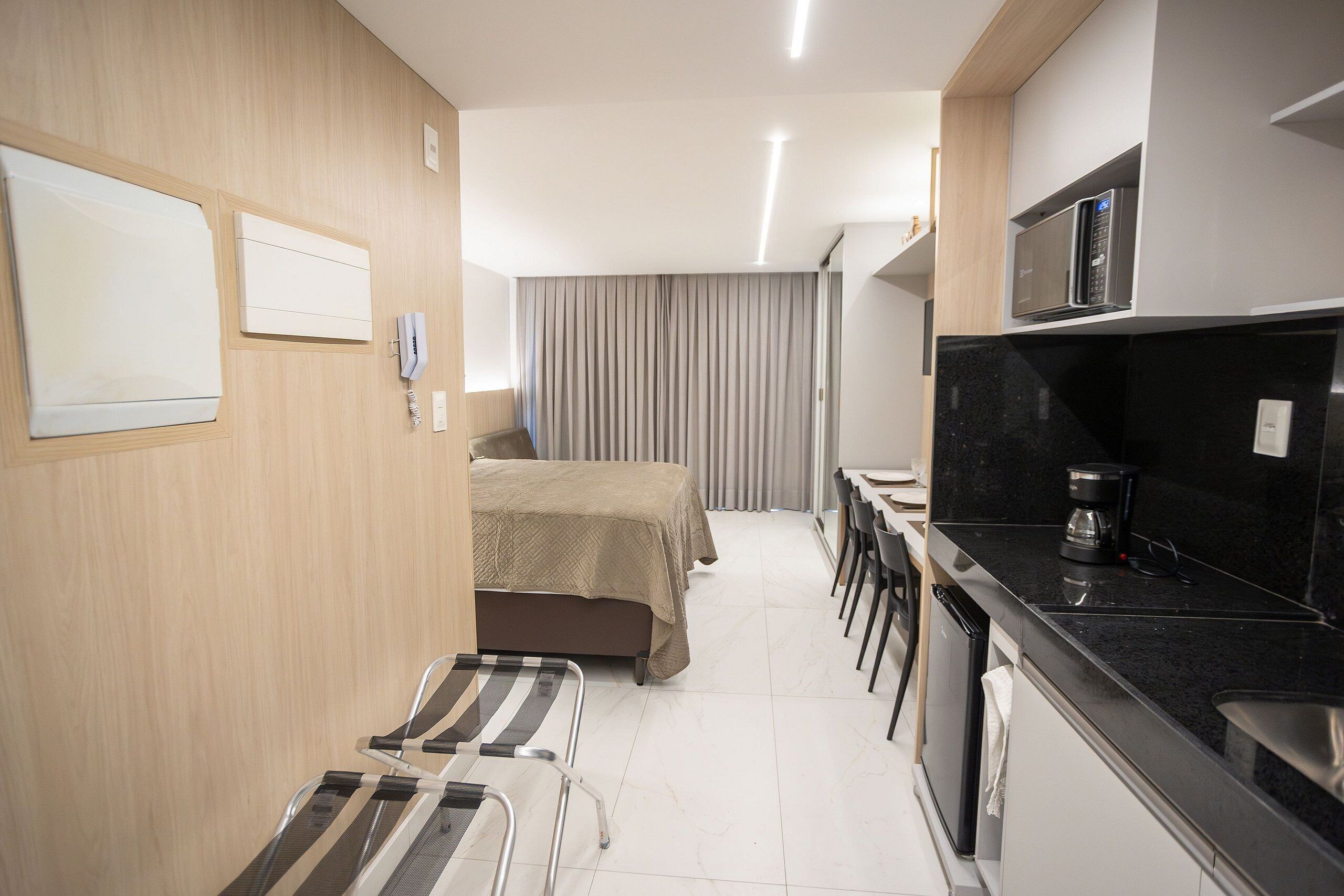 A compact hotel room with a bed, a small seating area, a kitchenette, and a bathroom.