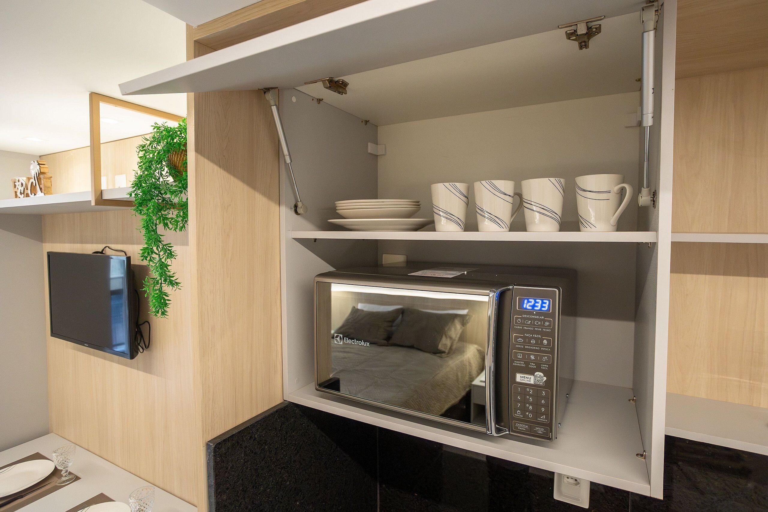 Une petite cuisine équipée d’un four à micro-ondes, d’étagères pour la vaisselle et d’un téléviseur.
