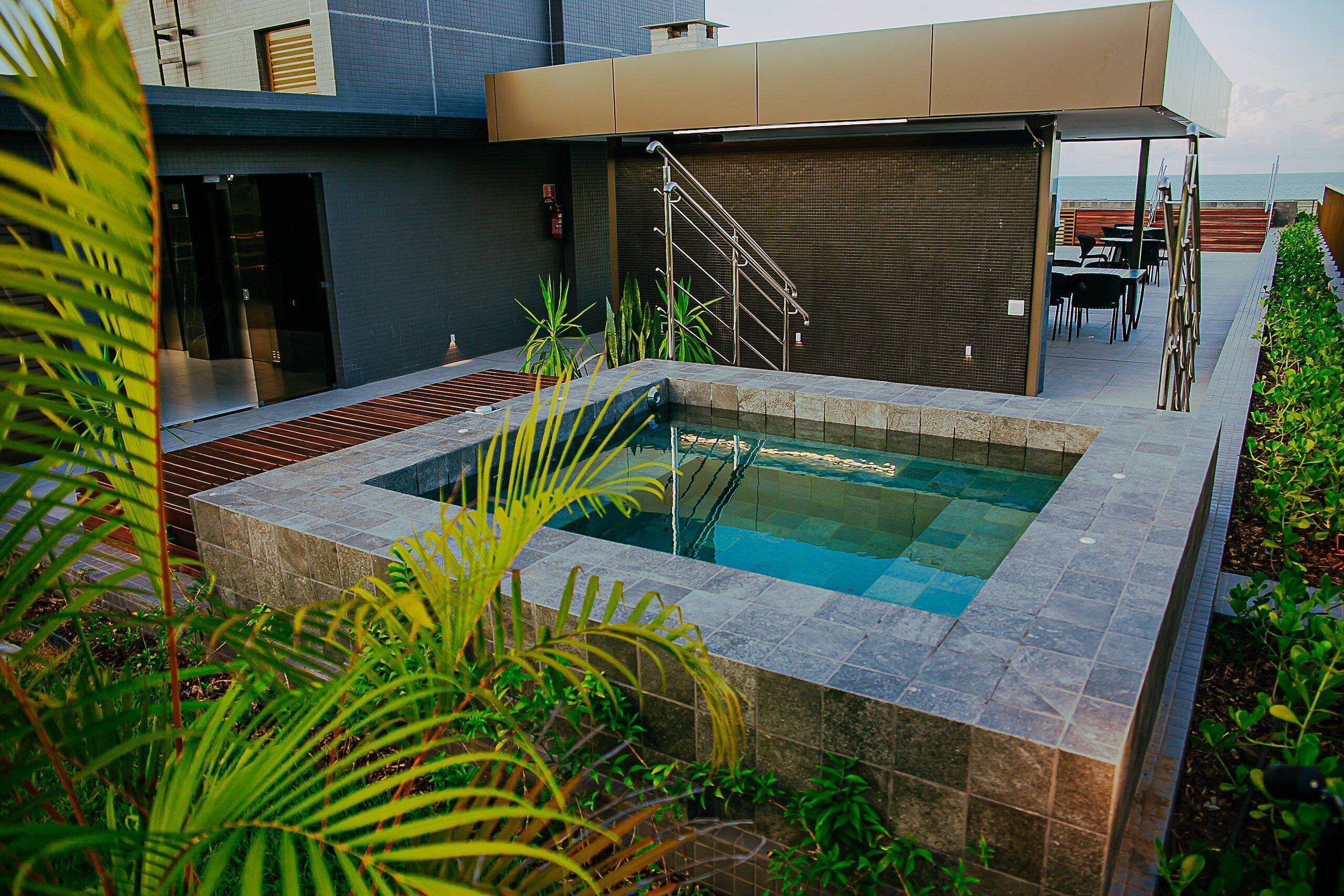 Un'area piscina moderna all'aperto con bordi in pietra, una scala e vista sul mare.
