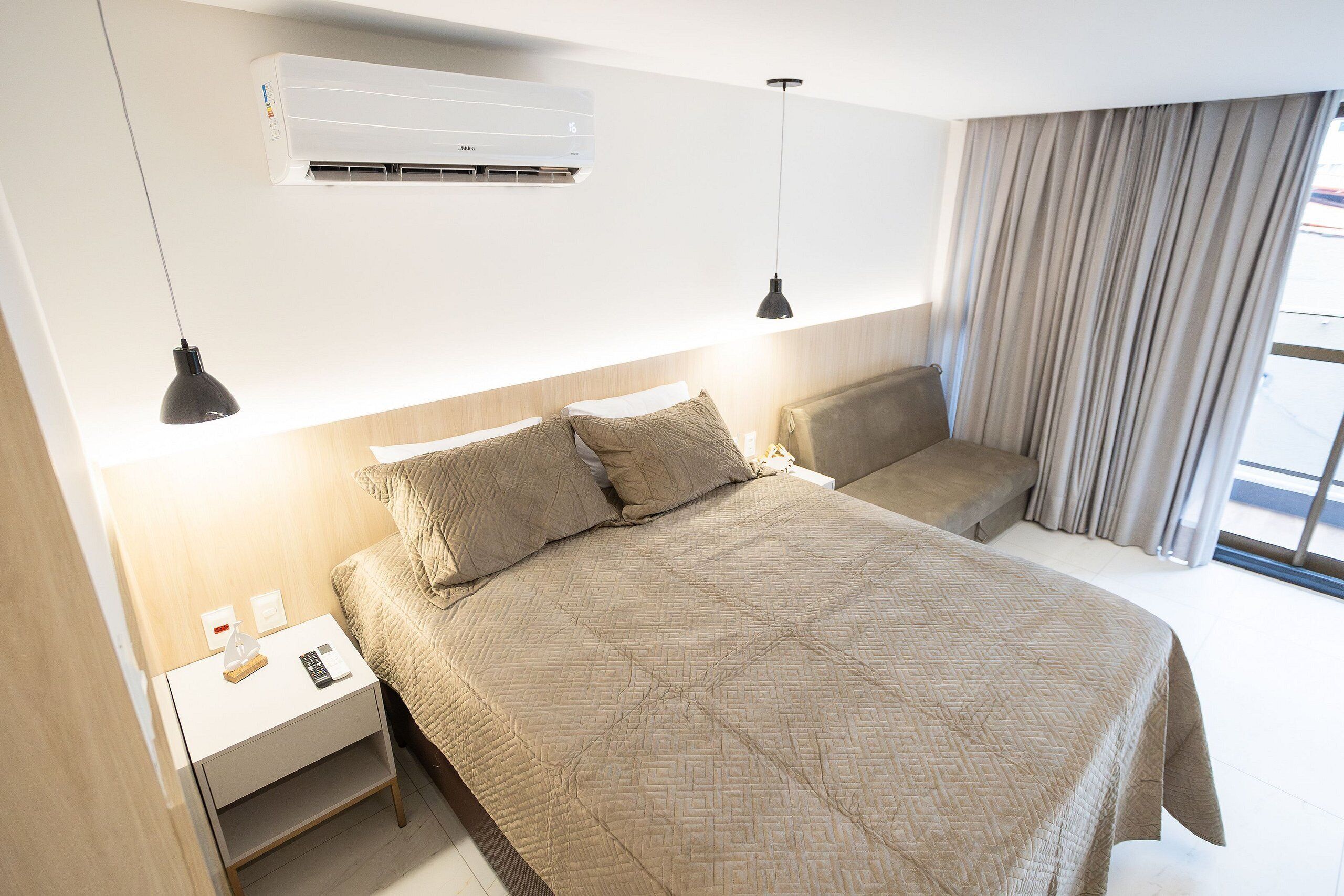 A hotel room with a bed, bedside tables, an air conditioner, and a window with curtains.