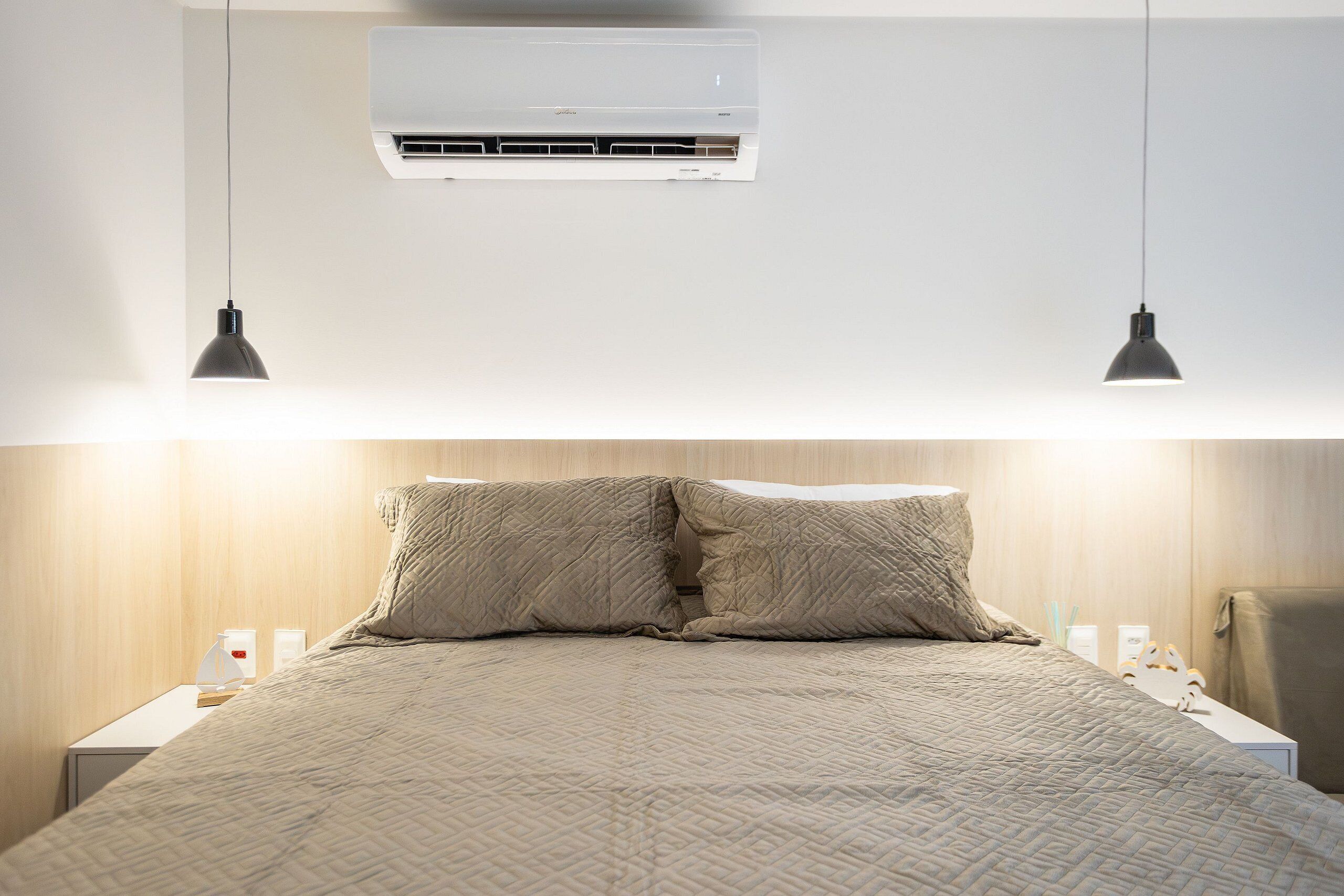 Ein ordentlich bezogenes Bett mit einer gesteppten Decke, einer Wand-Klimaanlage und zwei Pendelleuchten.