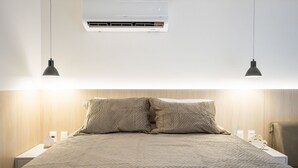 A neatly made bed with a quilted cover, a wall-mounted air conditioner, and two pendant lights. - Unity #222 a Few Steps From the Beach by Carpediem (João Pessoa)