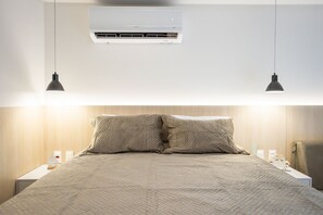 Ein ordentlich bezogenes Bett mit einer gesteppten Decke, einer Wand-Klimaanlage und zwei Pendelleuchten.
