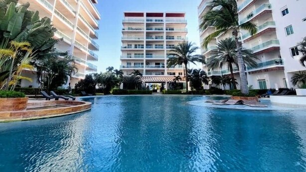 Ein modernes Hotel mit einem zentral gelegenen Schwimmbad, umgeben von Palmen und anderer Bepflanzung.