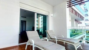 Ein Balkon mit zwei weißen Liegestühlen und einer Glastrennwand.