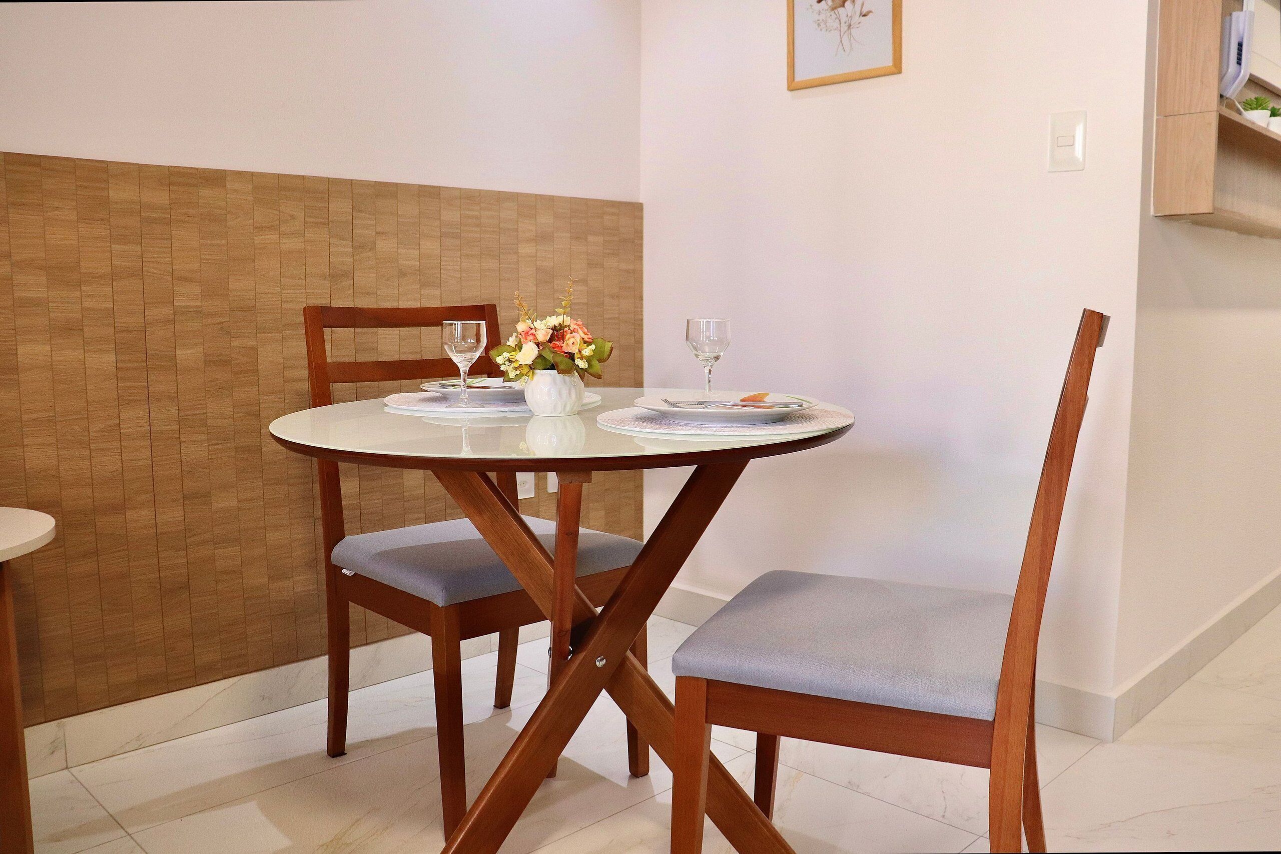 A dining area with a round table, two chairs, a vase with flowers, and a wine glass.