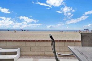 Une vue sur la plage avec un espace patio comprenant une table et des chaises, un mur de briques et des parasols au loin.