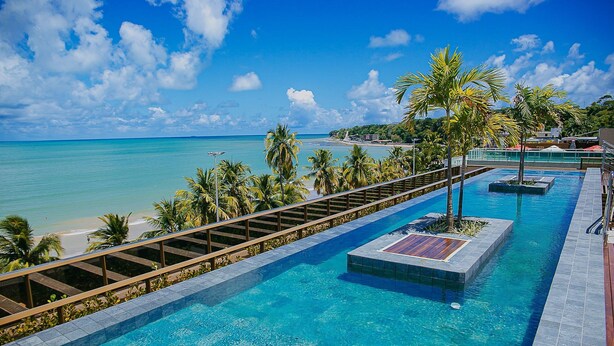 Una piscina con agua azul cristalina, rodeada de palmeras y vista a la playa.