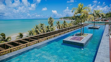 Una piscina con agua azul cristalina, rodeada de palmeras y vista a la playa.