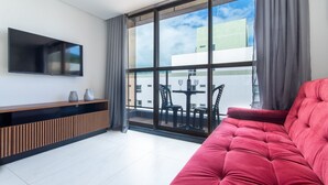 Una sala de estar moderna con un sofá rojo, un televisor de pantalla plana montado en la pared y un balcón con mobiliario exterior.