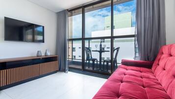 Una sala de estar moderna con un sofá rojo, un televisor de pantalla plana montado en la pared y un balcón con mobiliario exterior.