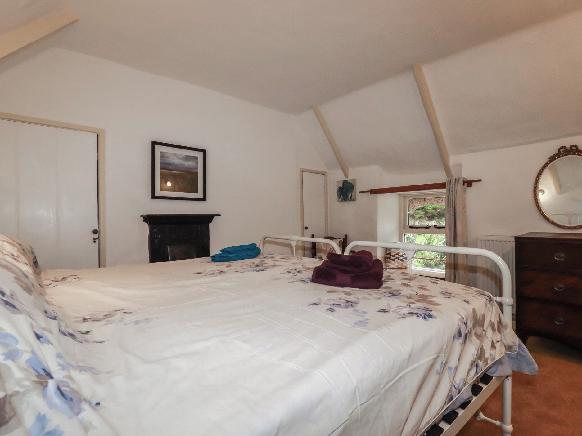 Een slaapkamer met een bed, een dressoir, een spiegel en een open haard.