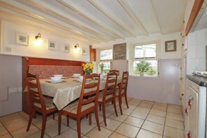 A dining area with a table set for four, wooden chairs, a bench, and a view of the outdoors through a window. - Plenteth (Truro)