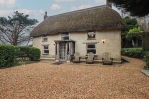 A thatched-roof house with a gravel driveway and two wooden chairs outside. - Plenteth (Truro)