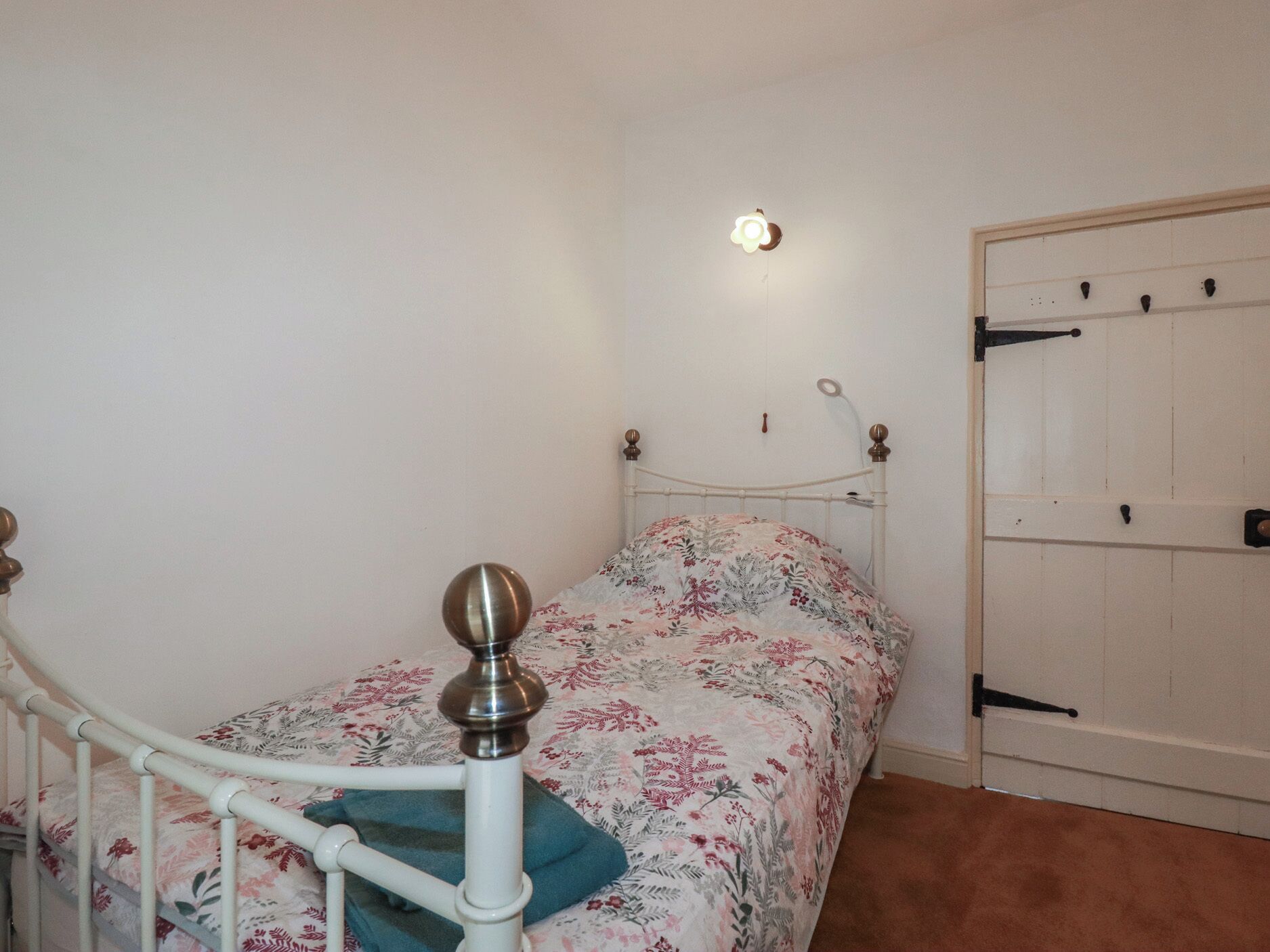 A bedroom with a single bed, a white door, and a wall-mounted light fixture.