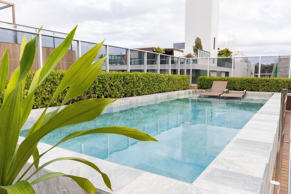 A modern outdoor pool area with a clear pool, a lounge chair, and a well-maintained hedge.