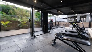 A gym with exercise equipment, including treadmills and weight machines, and a view of greenery outside. - Vivendas #404 - Apto em Cabo Branco by Carpediem (João Pessoa)