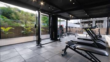 Un gimnasio con equipo de ejercicio, incluyendo cintas de correr y máquinas de pesas, y vista a zonas verdes exteriores.