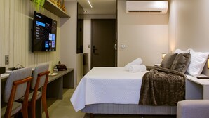 A hotel room with a bed, a desk with a computer, a TV, and an air conditioning unit. - Acqua Tambaú Prime - By Almare (João Pessoa)