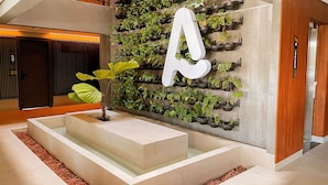 A modern interior with a large 'A' wall-mounted feature, a potted plant, and a seating area. - Acqua Tambaú Prime - By Almare (João Pessoa)