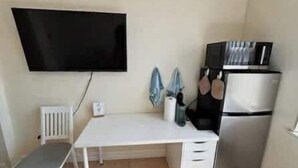 A small kitchenette with a white table, a chair, a flat-screen TV mounted on the wall, a refrigerator, and a microwave. - Cozy Studio – Free Bikes – 1 Mi to Beach (Bonita Springs)