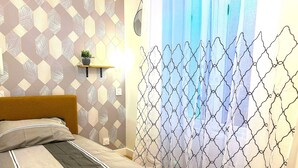 Uma cama bem arrumada com cabeceira, uma mesinha de cabeceira com uma planta e um papel de parede estampado.