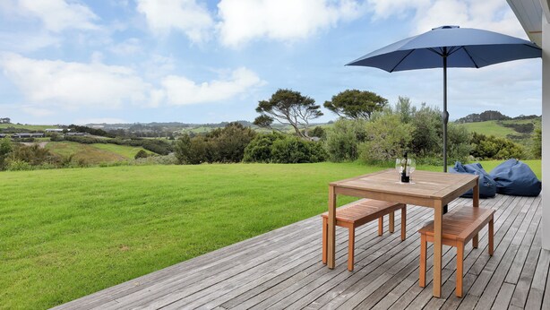 En træterrasse med et bord, bænke, en parasol og udsigt over et græsland med træer.