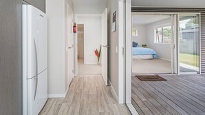 A hallway leading to a bedroom with a bed, a window, and a door to a balcony. - Soleil Studio - Whangamata Self-contained Unit (Whangamata)