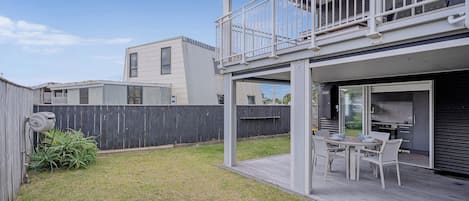 A modern two-story house with a balcony, a patio with outdoor furniture, and a fenced backyard.