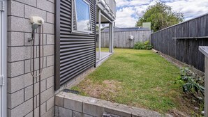 A residential backyard with a fenced area, a small lawn, and a wooden deck. - Soleil Studio - Whangamata Self-contained Unit (Whangamata)