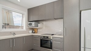 A modern kitchen with grey cabinets, a built-in microwave, oven, and a stainless steel refrigerator. - Soleil Studio - Whangamata Self-contained Unit (Whangamata)