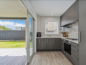 A modern kitchen with grey cabinets, a built-in microwave, and a window with blinds. - Soleil Studio - Whangamata Self-contained Unit (Whangamata)