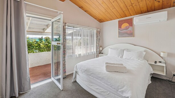Una camera da letto con un grande letto, una porta vetrata scorrevole su un balcone e una ventola a soffitto.