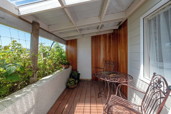 Une terrasse en bois avec une table et des chaises en métal, entourée de plantes en pot et offrant une vue sur la verdure.