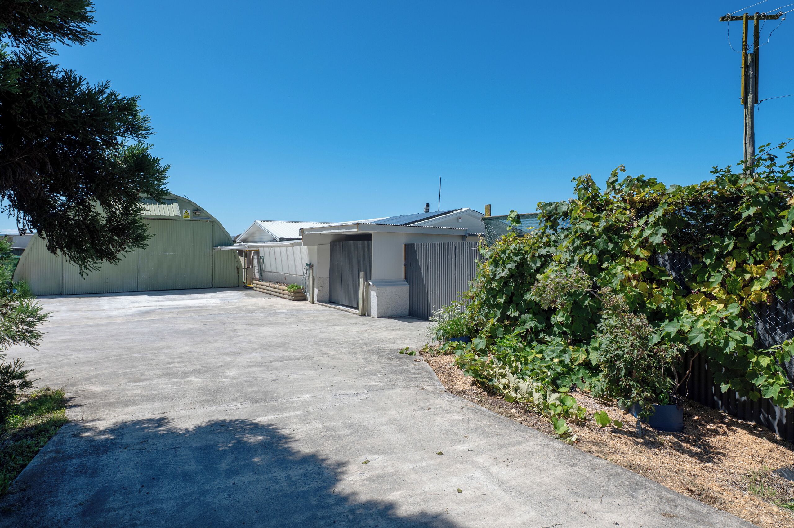 A concrete driveway leading to a building with a covered parking area and a fenced garden.