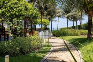 A paved pathway with a sign reading "CAMINHO SENSORIAL" surrounded by lush greenery and palm trees. - Paraiso do Atlantico #102d - Style by Carpediem (Cabedelo)