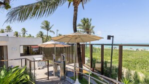 A modern outdoor area with a glass railing, palm trees, and umbrellas. - Paraiso do Atlantico #102d - Style by Carpediem (Cabedelo)
