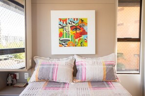 A bedroom with a bed, pillows, a window, a wall-mounted artwork, and a small statue. - Paraiso do Atlantico #102d - Style by Carpediem (Cabedelo)