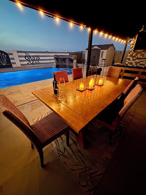 Un espace extérieur aménagé pour les repas, avec une piscine, des guirlandes lumineuses et un mur en pierre.