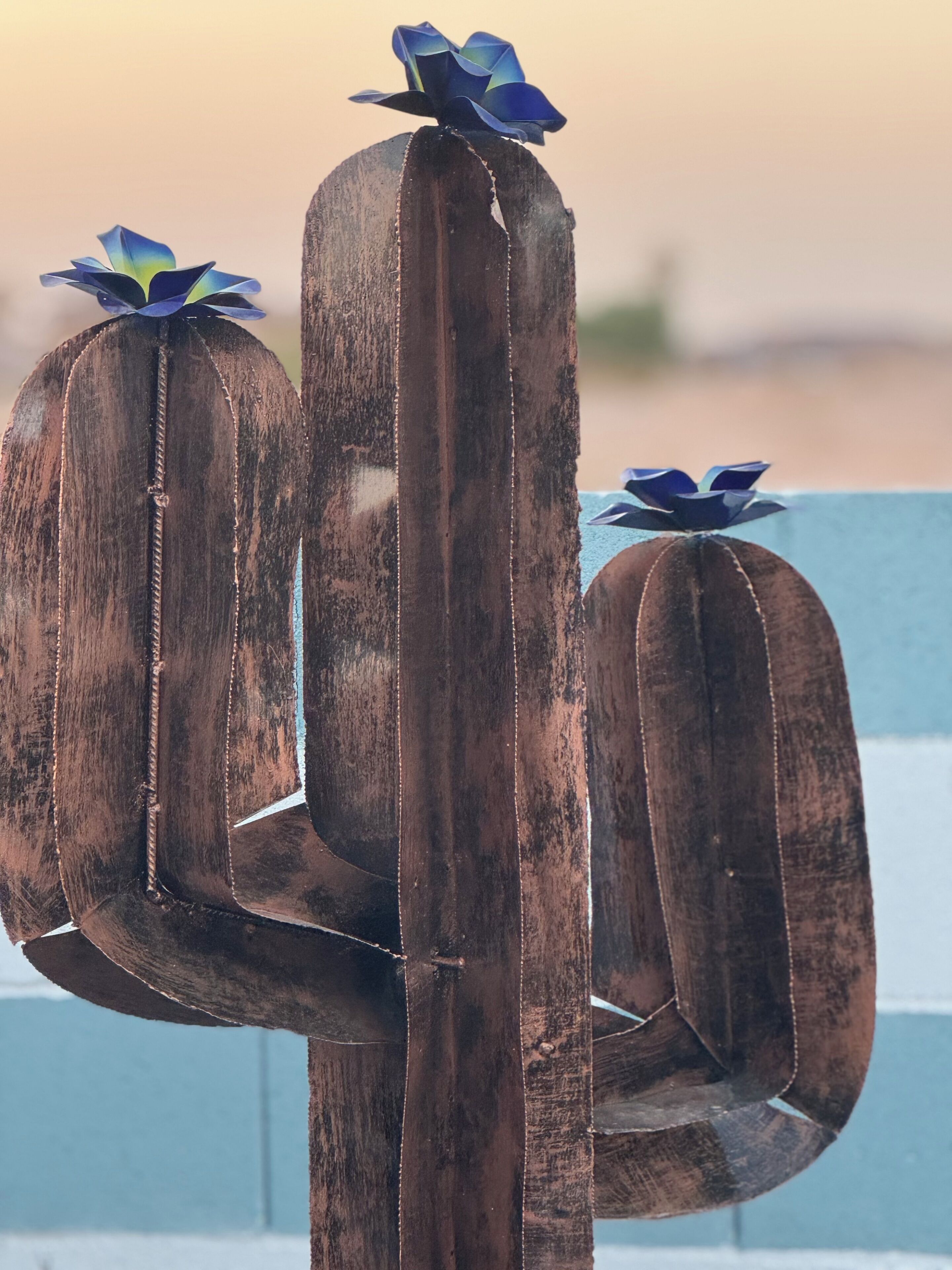 A cactus sculpture with a blue flower on top, set against a blurred background.