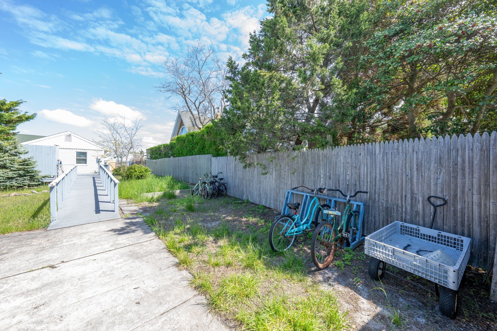 A concrete pathway leading to a wooden fence with bicycles and a wheelbarrow.