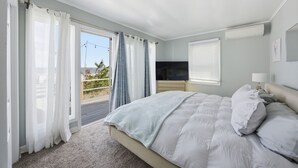 Une chambre à coucher avec un lit, un téléviseur, une fenêtre avec des rideaux et un appareil de climatisation.