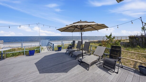 Une terrasse avec des sièges, un grand parasol et une vue sur l’océan.