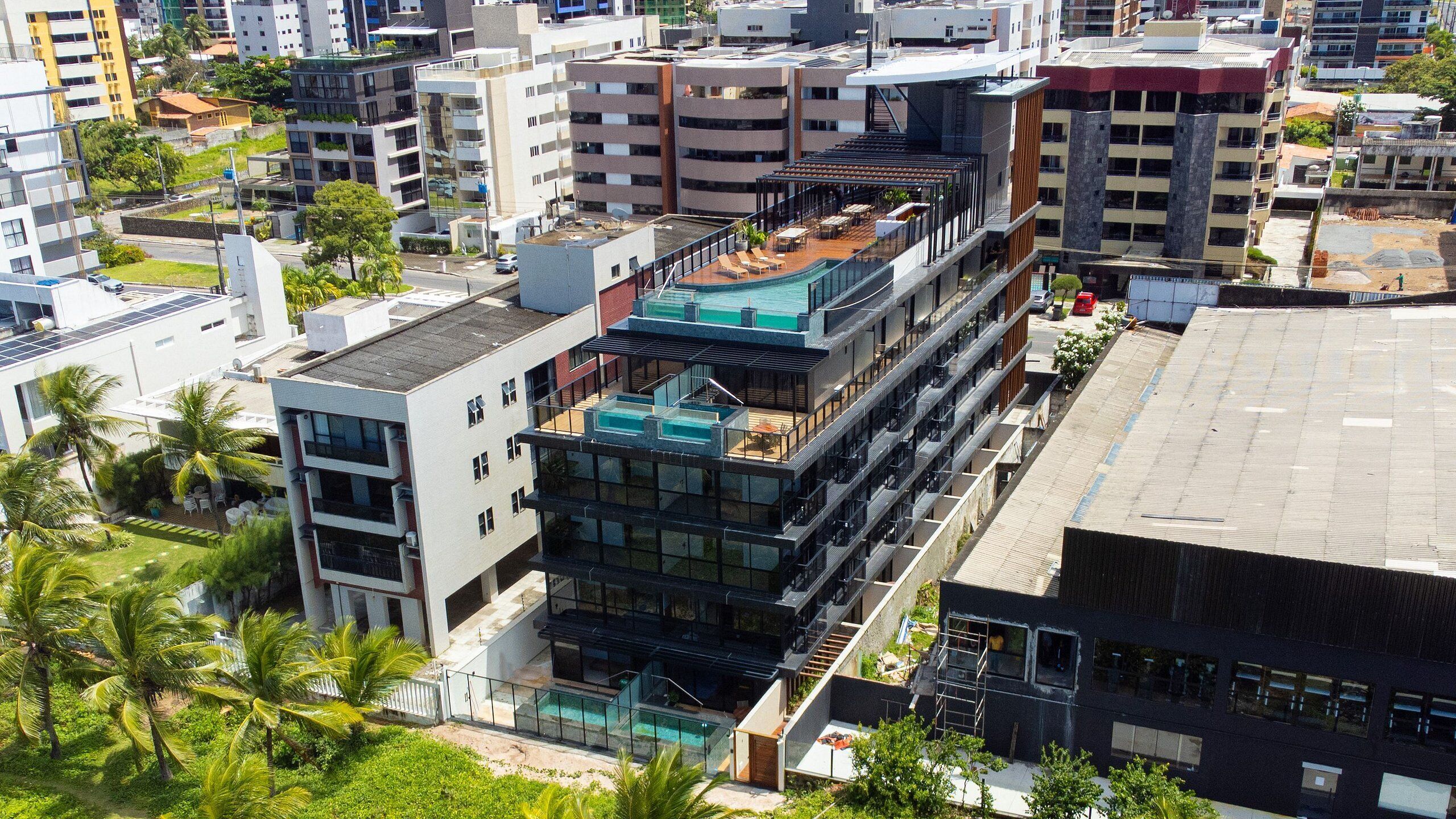 Un immeuble moderne à plusieurs étages, doté d’une piscine sur le toit, de balcons et d’une façade en verre.